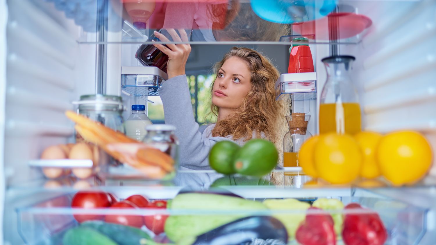 A woman taking a bottled juice out of the fridge.