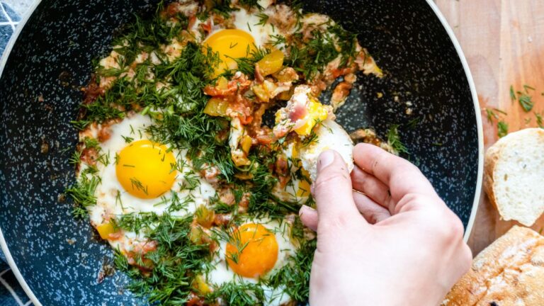 A hand dipping a piece of bread on an egg dish.