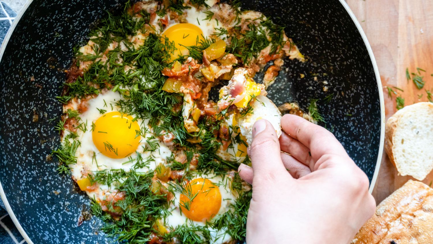 A hand dipping a piece of bread on an egg dish.