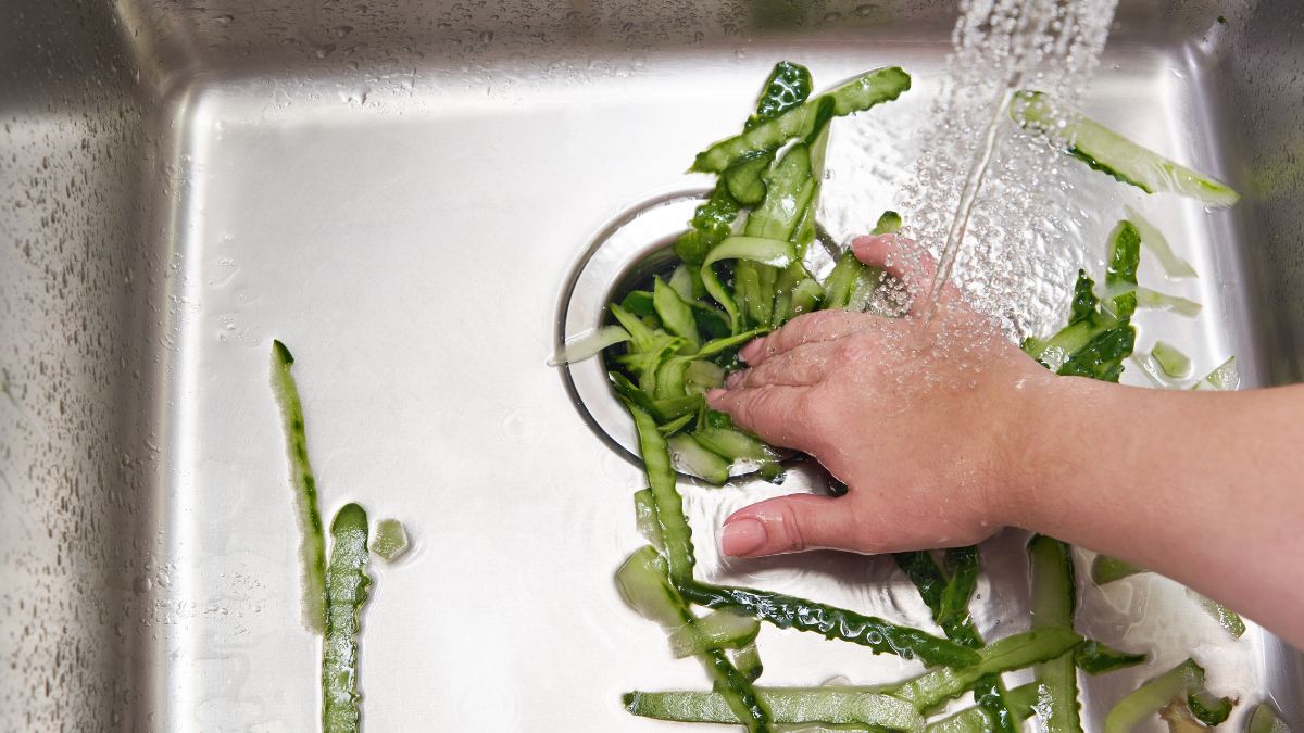 A hand pushing down vegetable peelings through a sink.