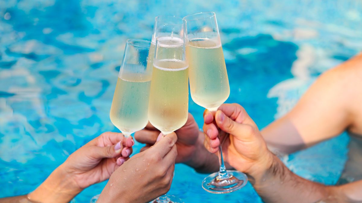 Four people's hands holding up a glass of champagne for a toast in a blue pool.