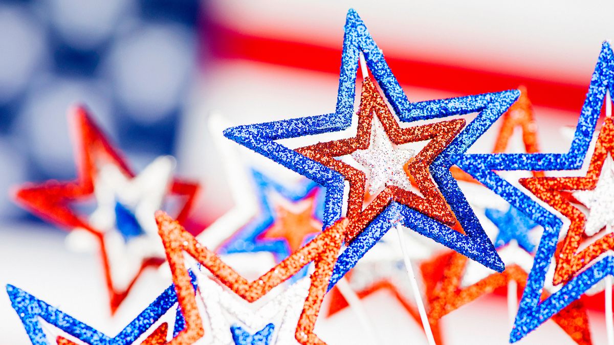 Focus shot on glittery stars in red, white and blue with the American flag just behind it.