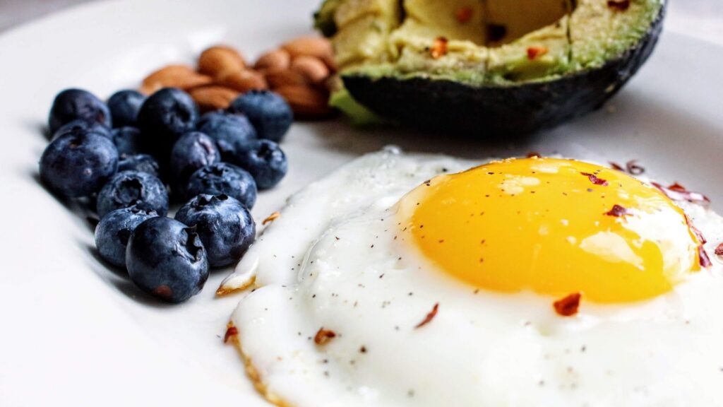 Closeup shot of a plate with sunny side up eggs, blueberries, avocado, almonds.