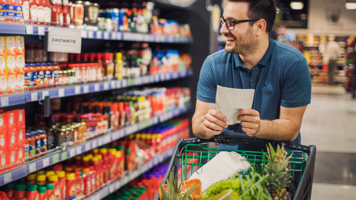 A man walking through a grocery isle while pushing his cart.