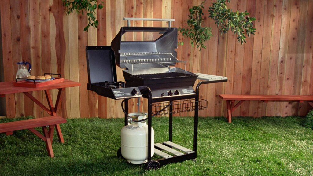 A gas grill in a backyard with a tall wooden fence behind it.