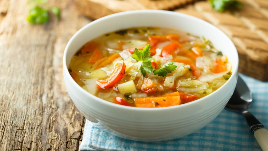 A bowl of vegetable soup on a wooden surface.