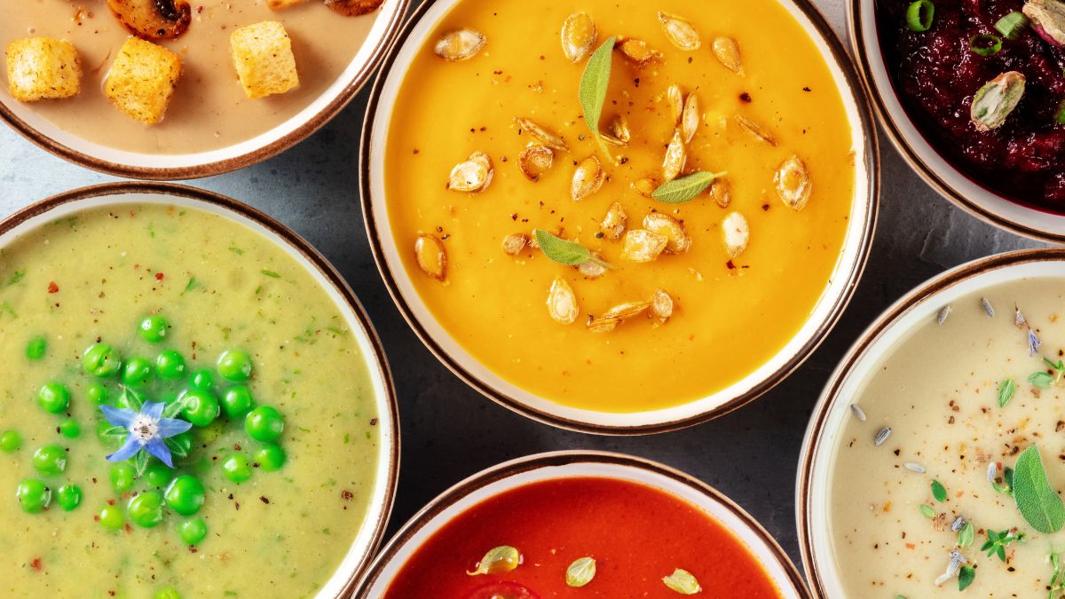 Flat lay shot of different bowls of soups, on a dark wood surface.