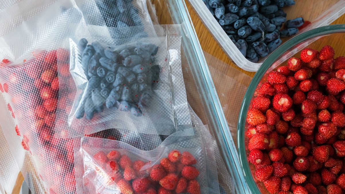 strawberries and blueberries in separate vacuum bags beside a big bowl of strawberries.