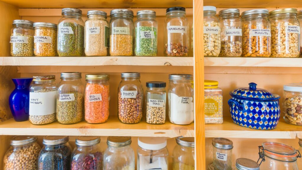 A wooden shelf with an assortment of beans and pulses, in individual glass jars.