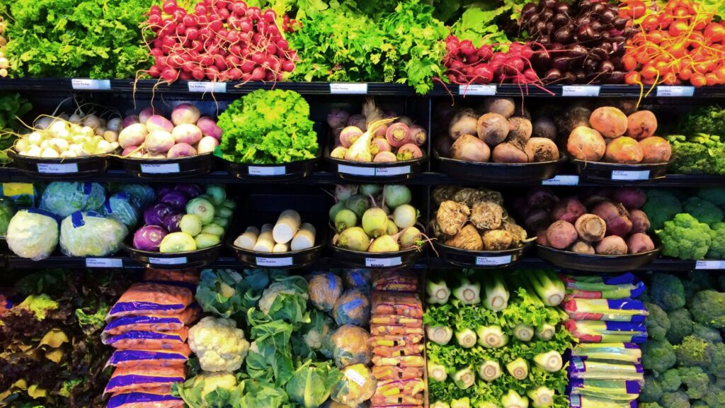 A shelf full of fall produce such as root vegetables, celery, and greens in a produce section in a grocery store.