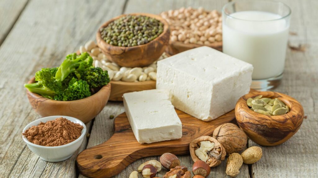 Ingredients such as tofu, seeds, various nuts, broccoli stallks and a bottle of milk. These ingredients are staples rich in protein.