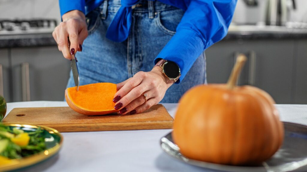 A person with manicured hands slicing a slice of pumpkin into smaller pieces.
