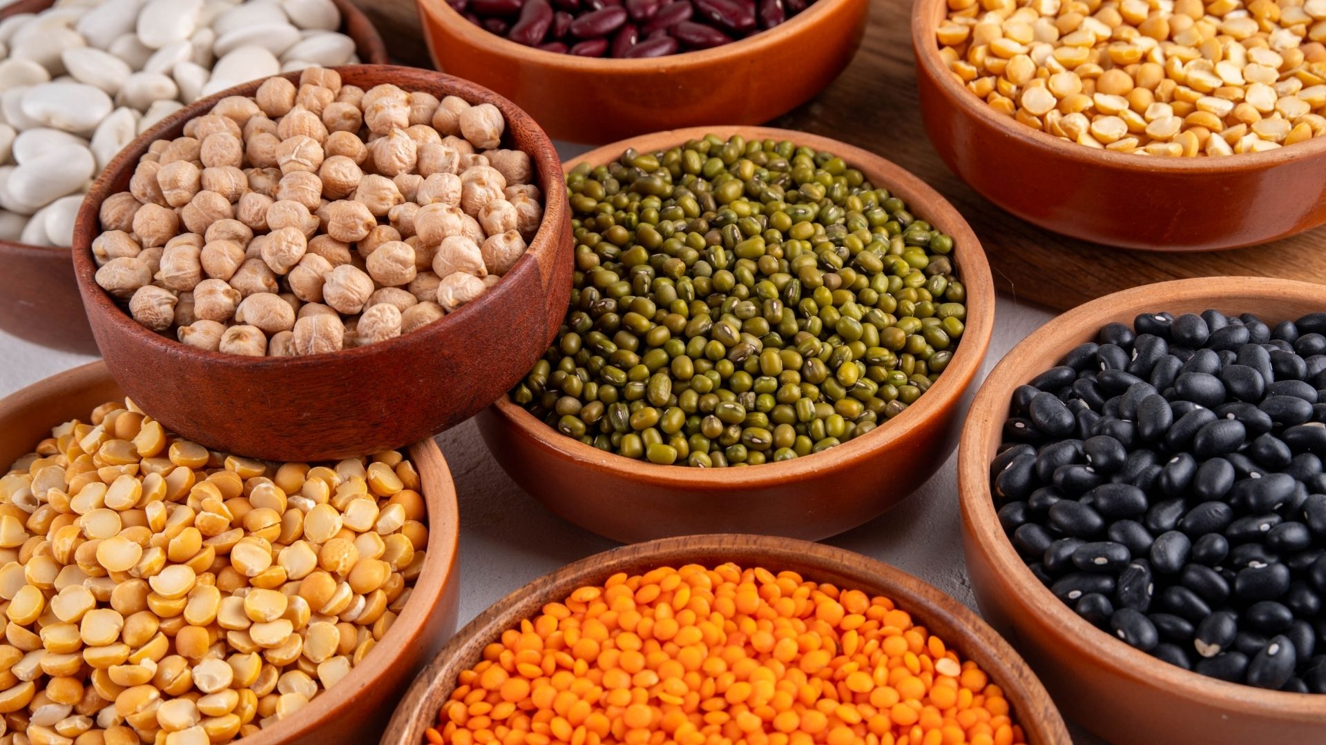 An assortment of dried beans in individual wooden bowls.