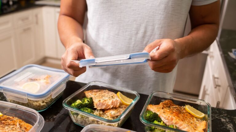 A person about to cover a container with meal prepped dish of salmon and vegetables. This article covers How to Meal Prep for Fall on a Budget