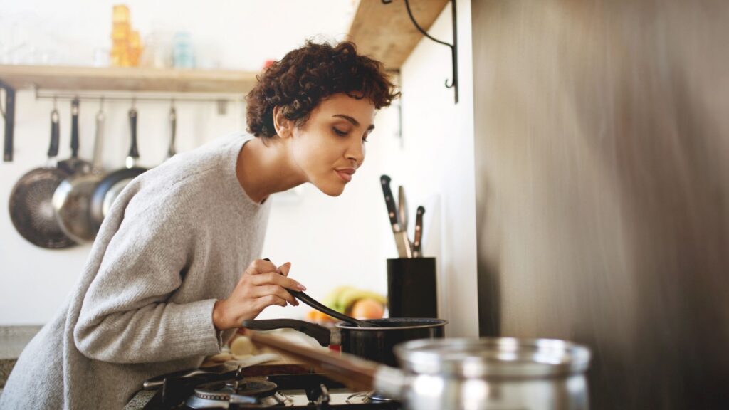 A woman cooking in the kitchen. Being intentional on what cooking method to use is one of the ways on How to Save Money on Heating Bills and Cooking Costs This Fall.