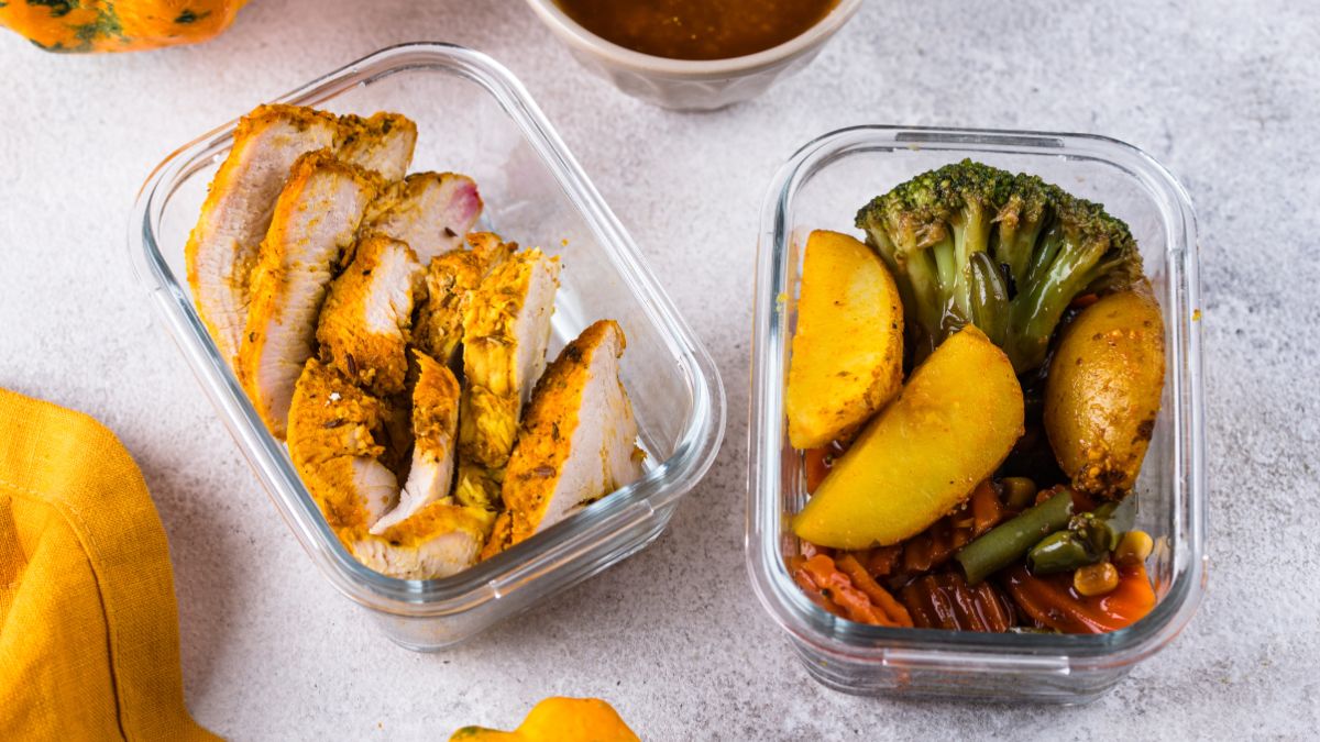 two glass containers, one with roasted chicken and the other with roasted vegetables, on a kitchen countertop.