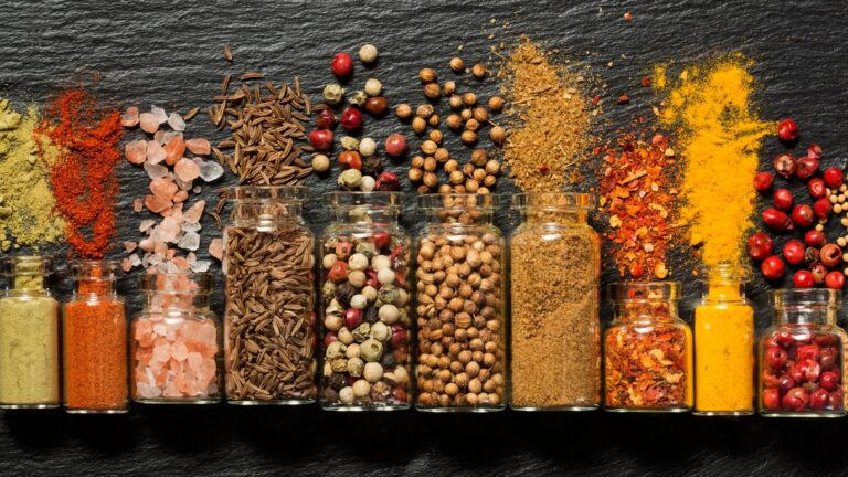 Flat lay shot of spice bottles each with spices on each of them, on a gray surface.