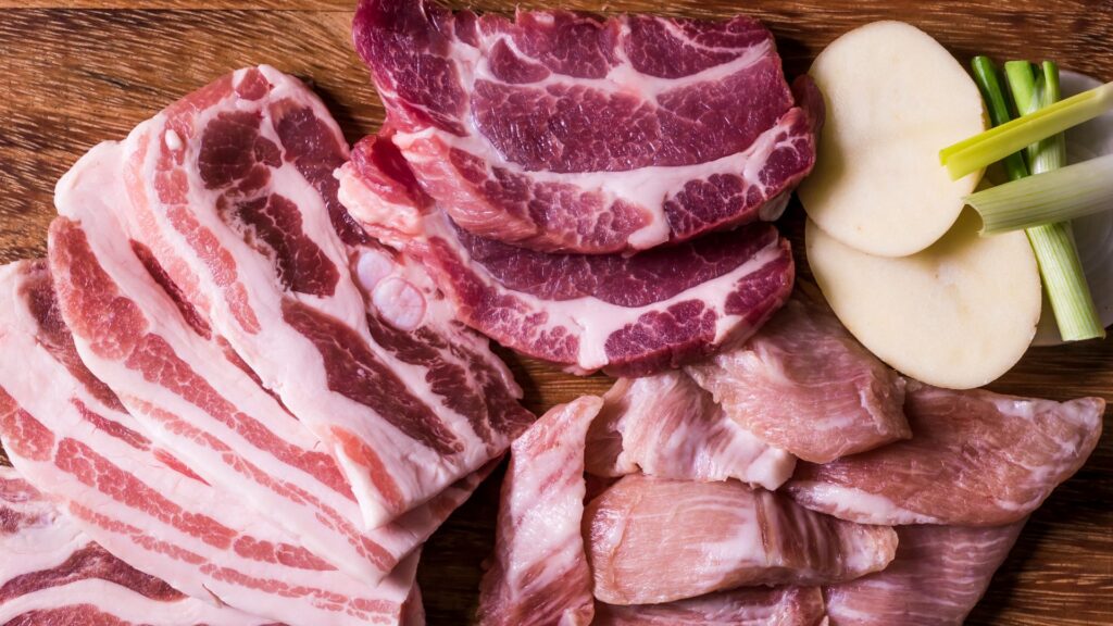 Flat lay shot of different cuts of pork on a wooden chopping board.