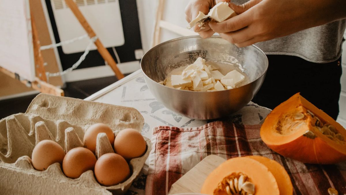 A person cutting butter into a mixing bowl for baking.