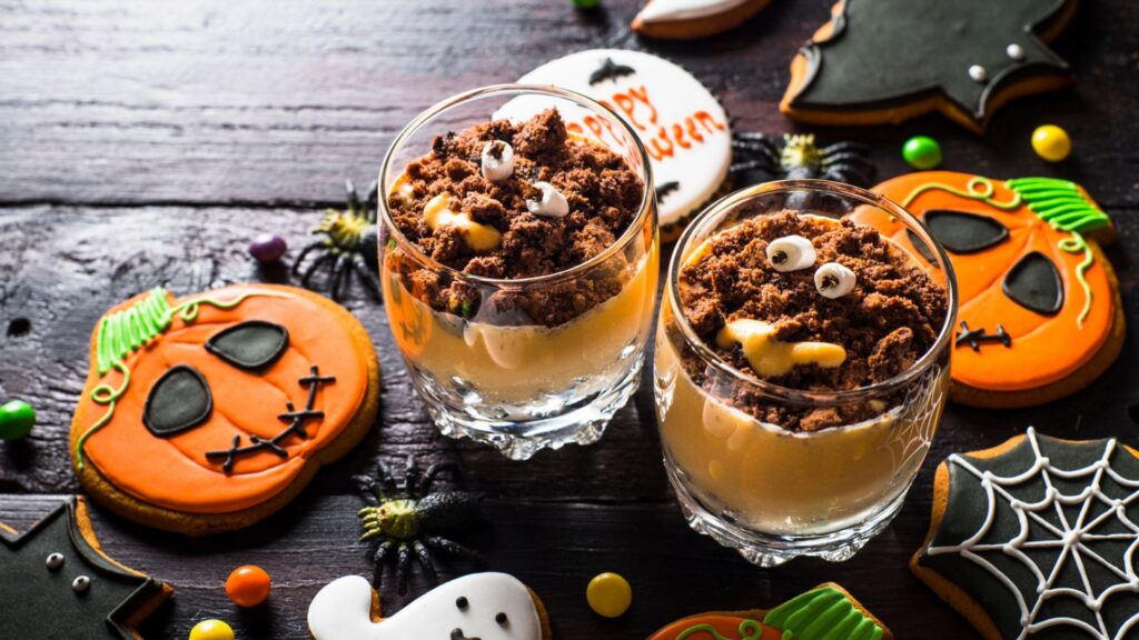 Halloween-themed desserts on a black wooden surface. Making use of what you already have when making Halloween party food is an excellent tip on the frugal cook's guide to Halloween food on a budget.