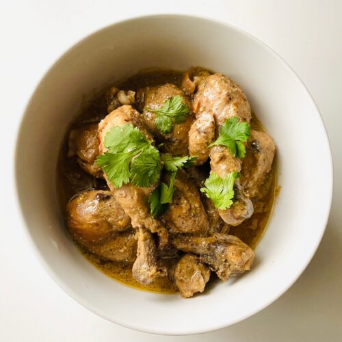 Bone-in chicken drumsticks and thighs braised in adobo sauce, served in a white bowl and garnished with fresh cilantro.