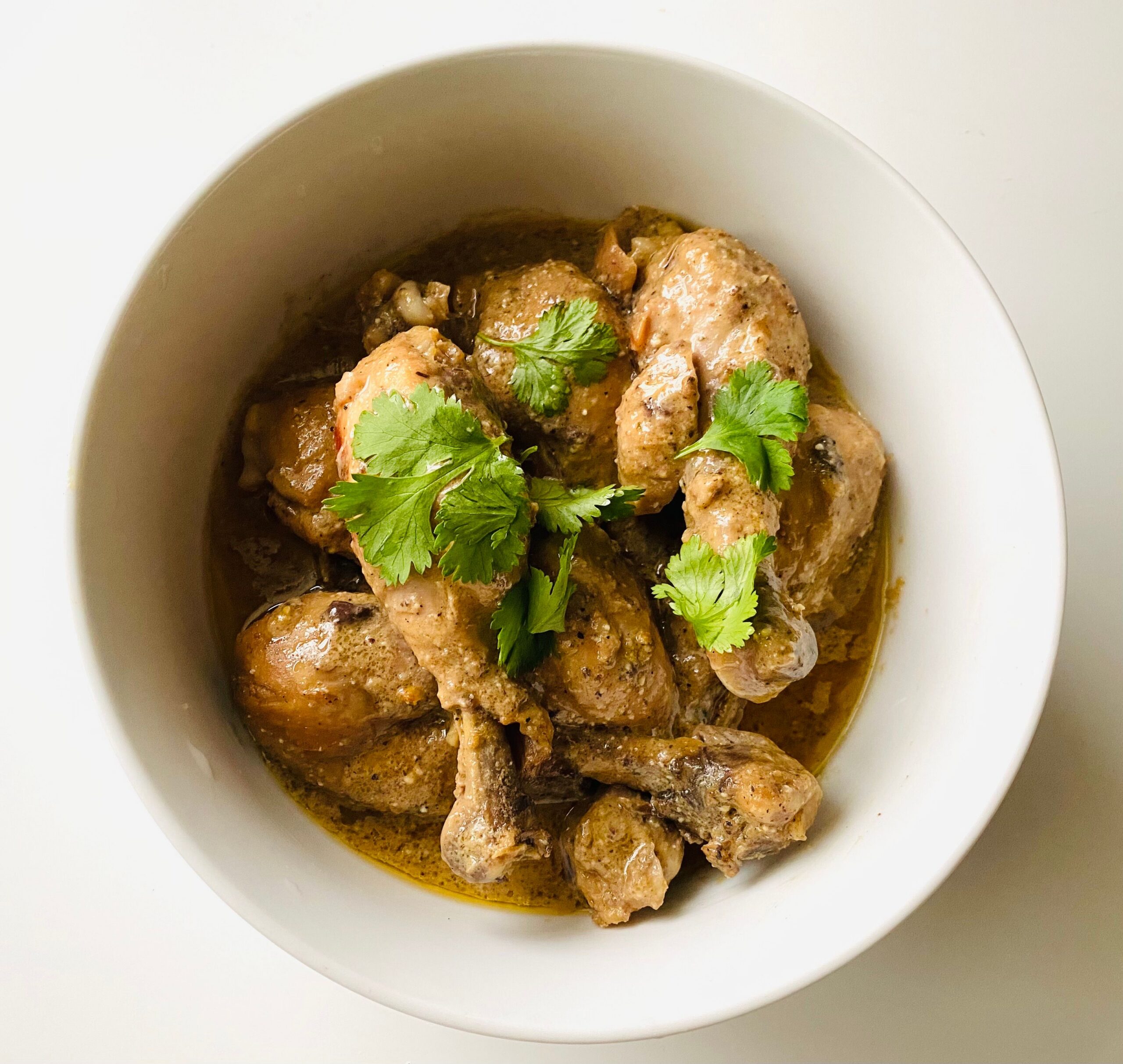 Bone-in chicken drumsticks and thighs braised in adobo sauce, served in a white bowl and garnished with fresh cilantro.