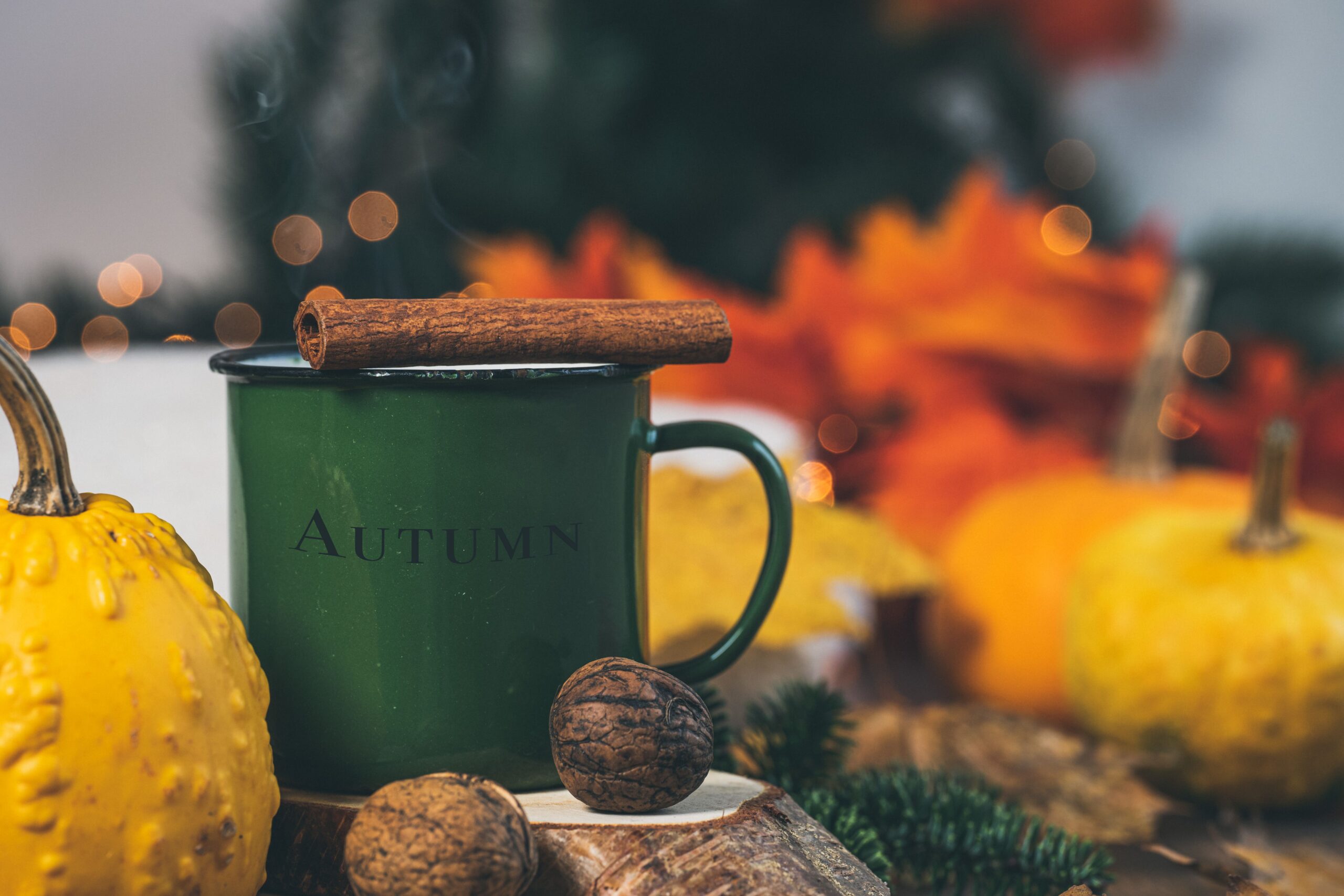 Fall spiced coffee in a green enamel mug with a cinnamon stick, surrounded by pumpkins