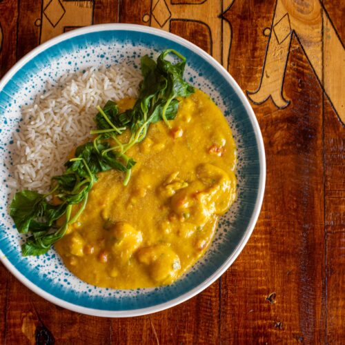 Close-up of curry dish with rice and greens on a wooden table, perfect for food photography.