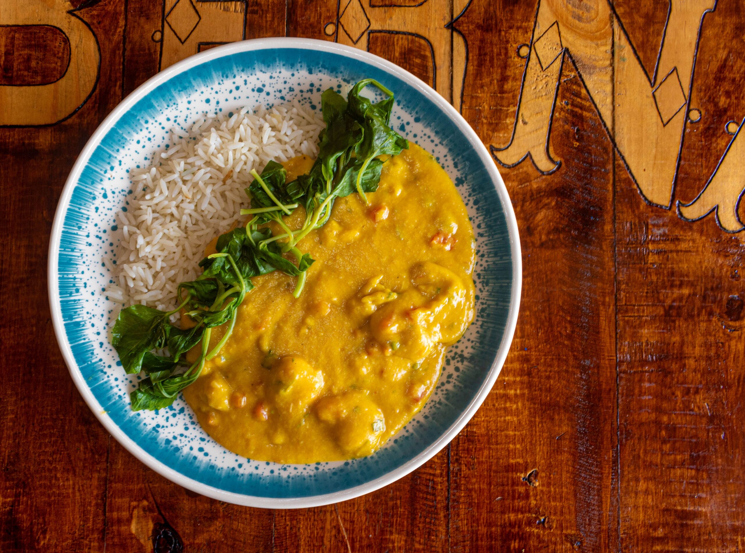 Close-up of curry dish with rice and greens on a wooden table, perfect for food photography.