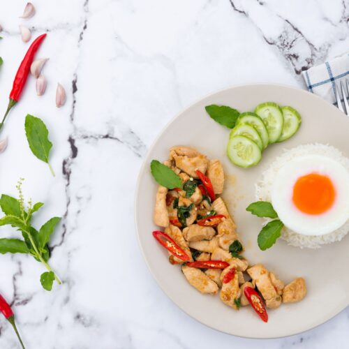 Delicious Thai basil chicken with rice and fried egg, styled on marble.