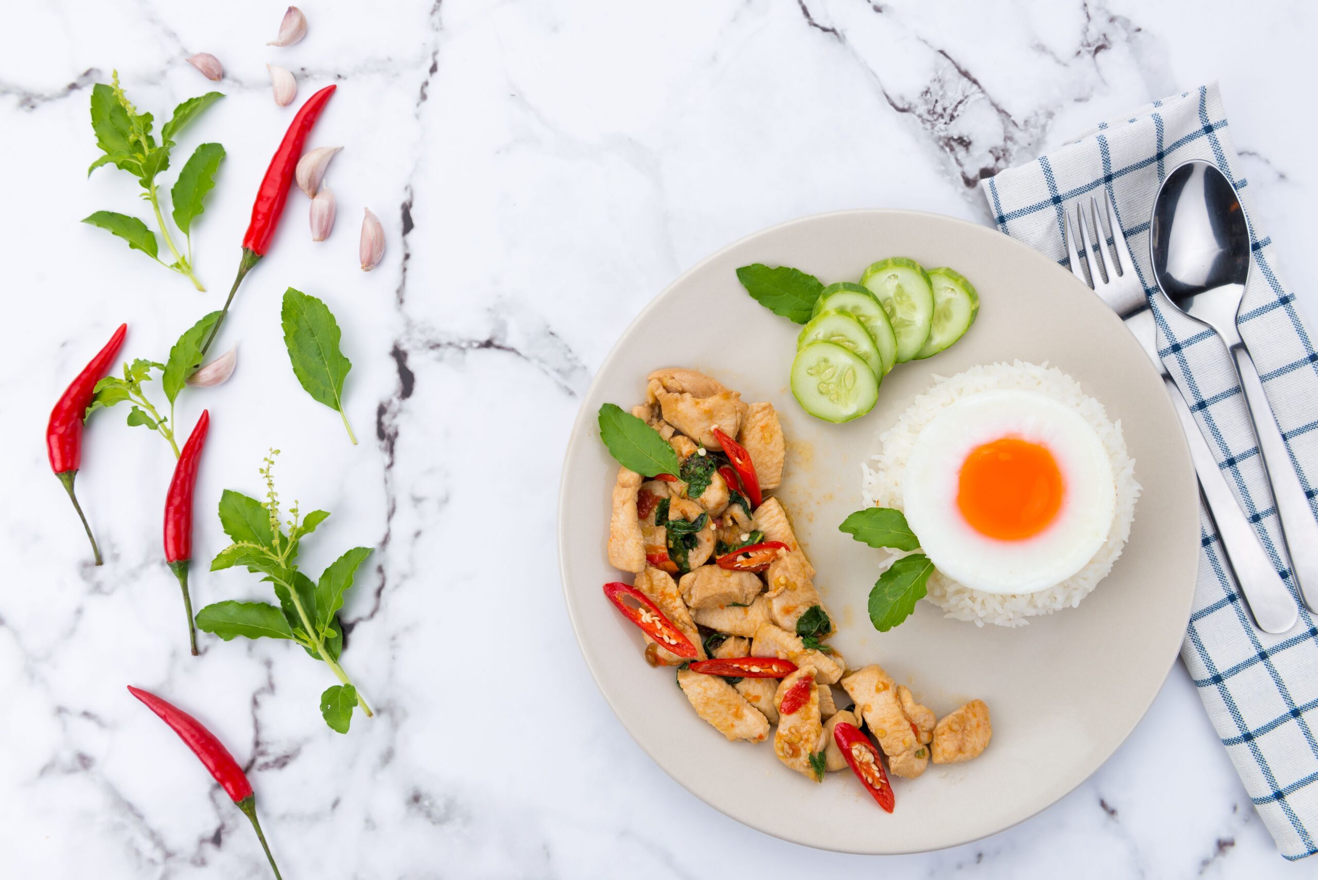 Delicious Thai basil chicken with rice and fried egg, styled on marble.