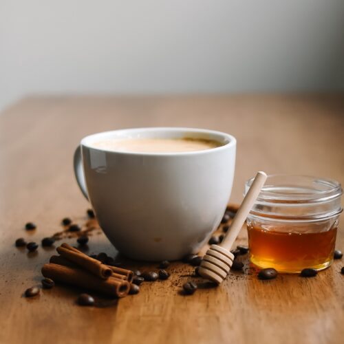 Chai latte made from homemade chai concentrate, in a white cup with cinnamon sticks and honey