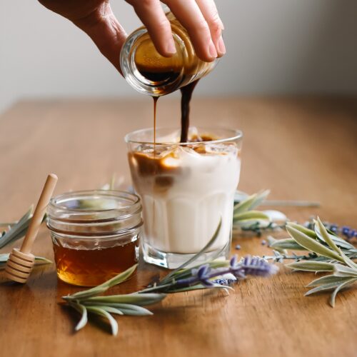 Coffee poured over homemade maple vanilla creamer in a glass, with a jar of honey alongside