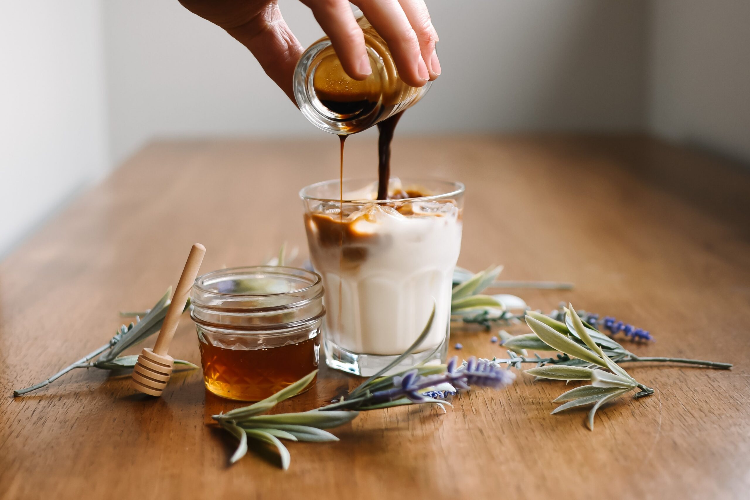 Coffee poured over homemade maple vanilla creamer in a glass, with a jar of honey alongside