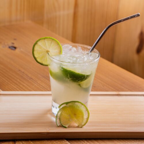 Tall citrus highball over ice with lime wheels, served on a wooden tray