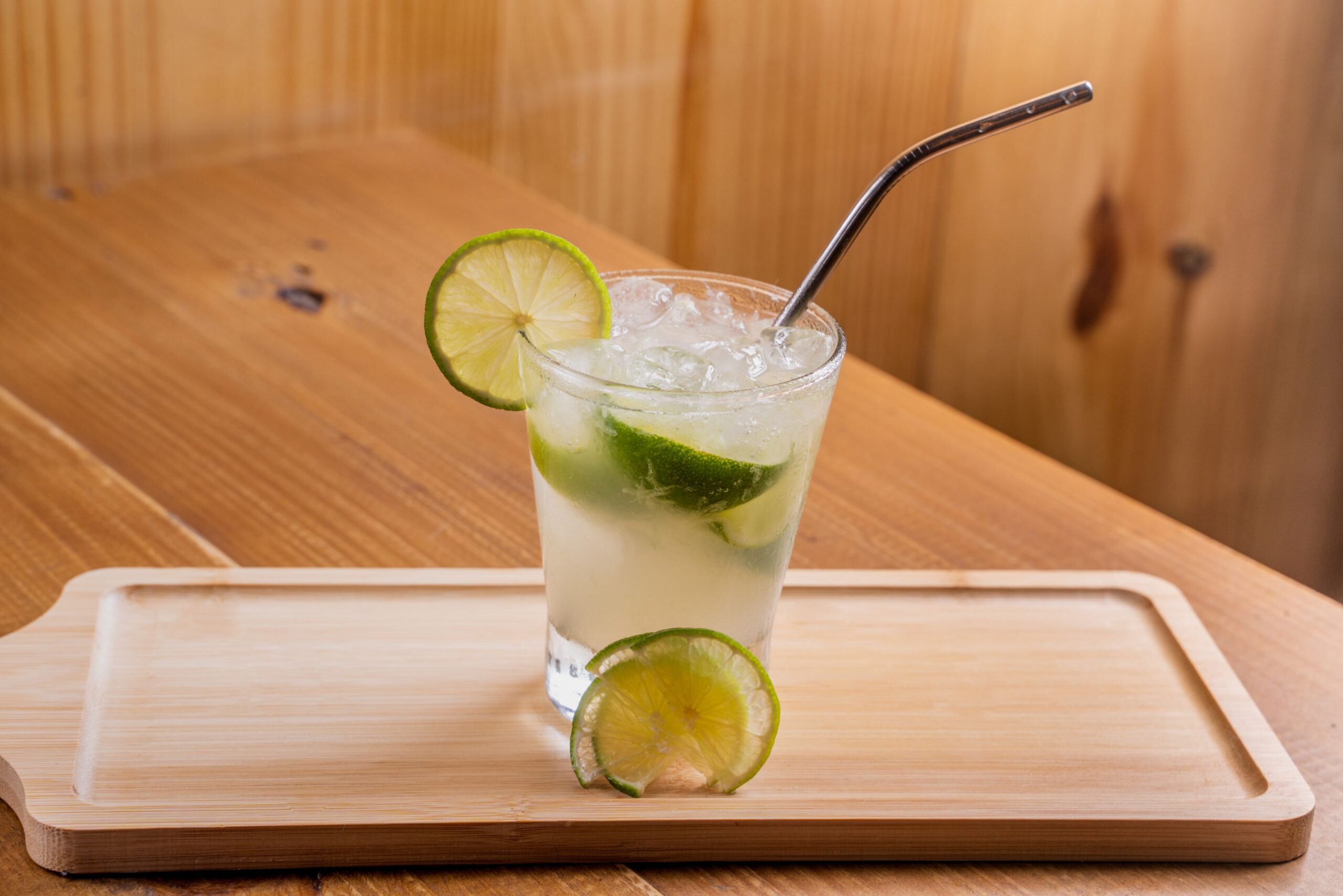 Tall citrus highball over ice with lime wheels, served on a wooden tray