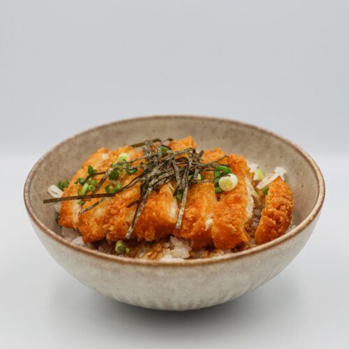 A mouthwatering chicken katsu served on steamed rice with savory toppings in a bowl.