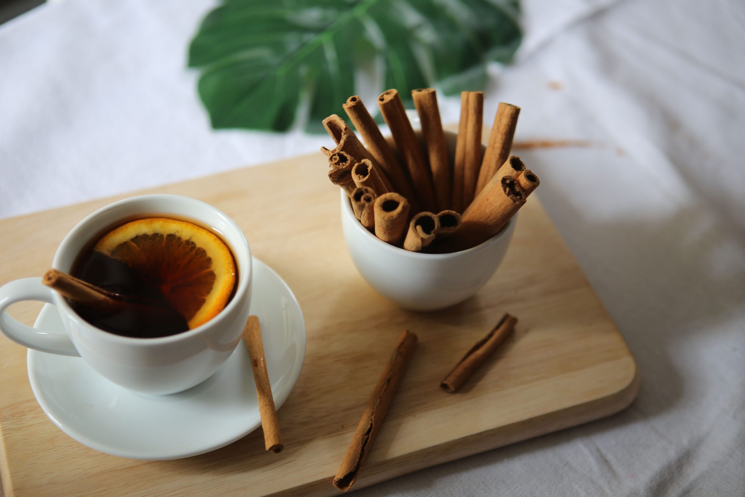 Spiced mulled apple cider in a white cup with an orange slice, beside a bowl of cinnamon sticks
