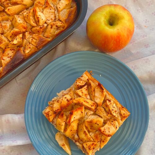 Baking dish of golden baked apple French toast with a whole apple beside it