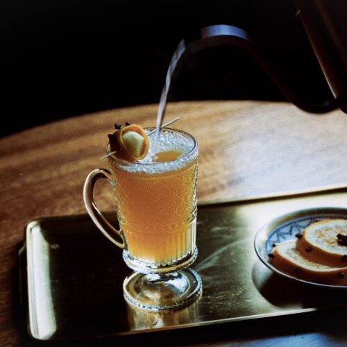 Warm spiced buttered rum in a glass mug with a cinnamon stick, served on a tray