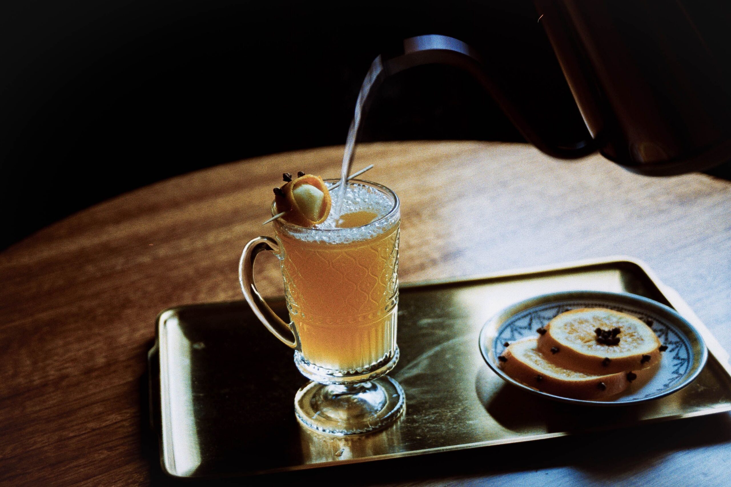 Warm spiced buttered rum in a glass mug with a cinnamon stick, served on a tray