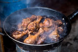 Close-up of juicy smoked chicken drumsticks cooking in a pan, creating mouthwatering steam.