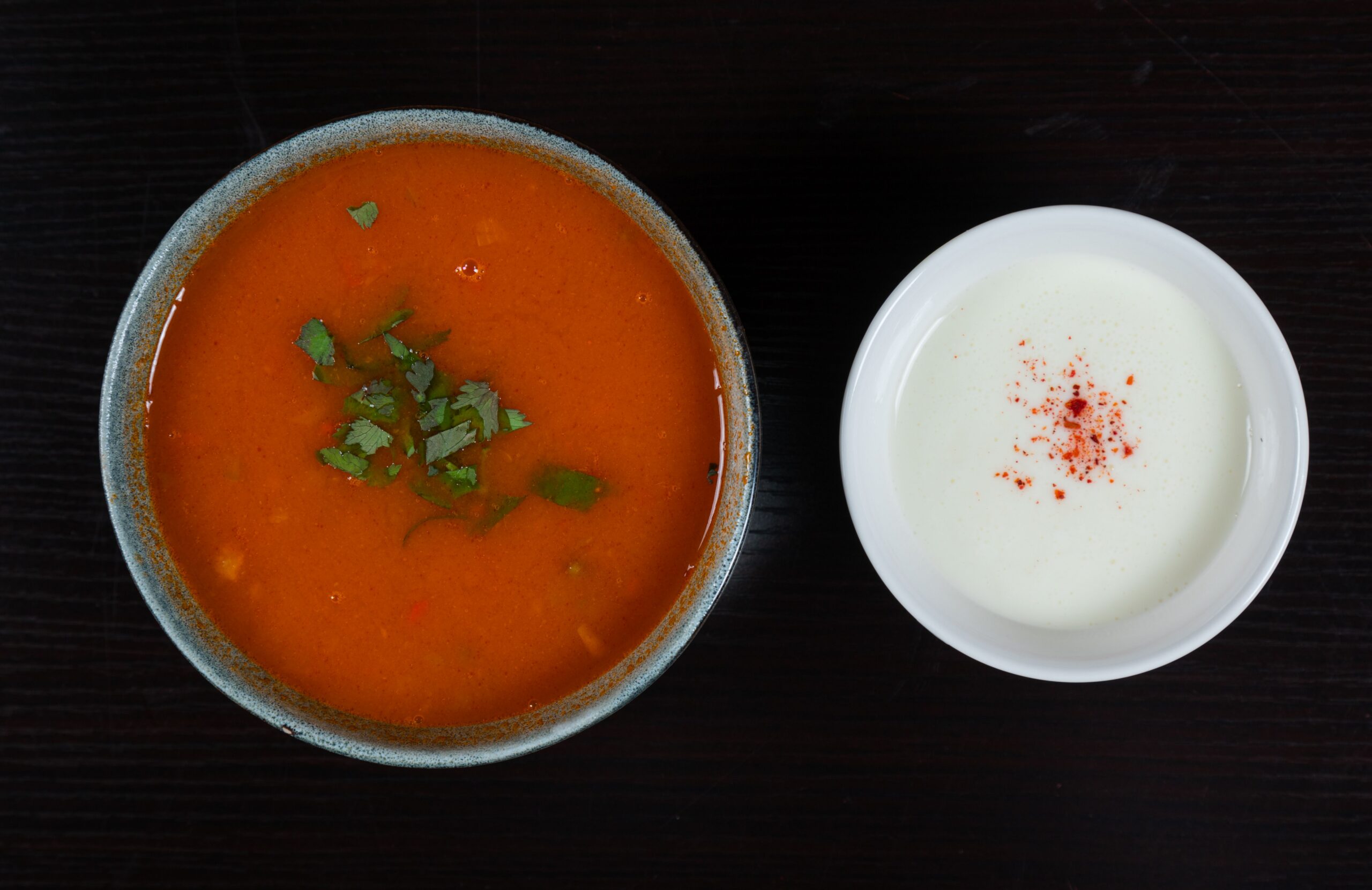A bowl of tomato soup garnished with cilantro, served alongside yogurt and paprika.