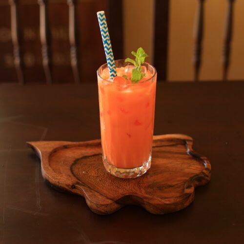 Tall glass of orange Thai iced tea over ice with a mint garnish on a carved wooden tray