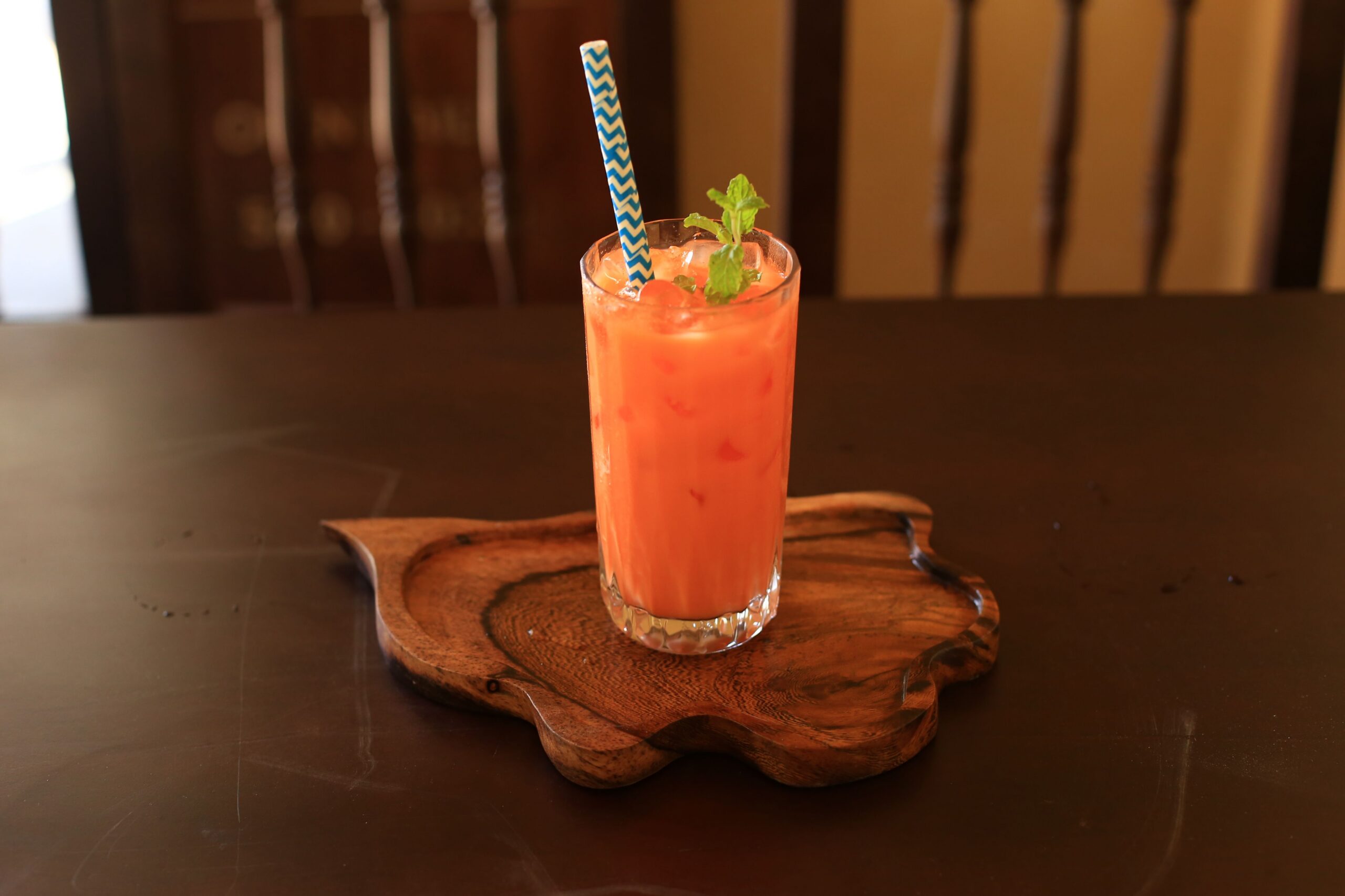 Tall glass of orange Thai iced tea over ice with a mint garnish on a carved wooden tray