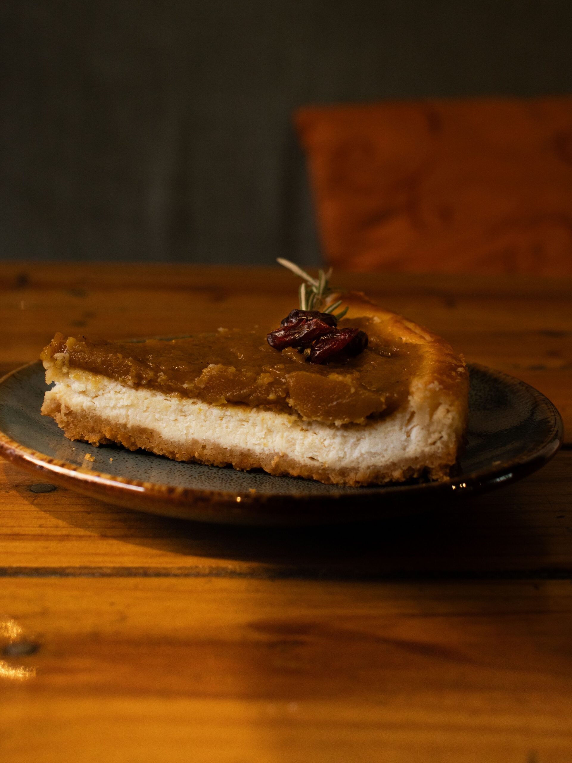 A slice of pumpkin cheesecake on a graham cracker crust, topped with cranberries and served on a dark plate