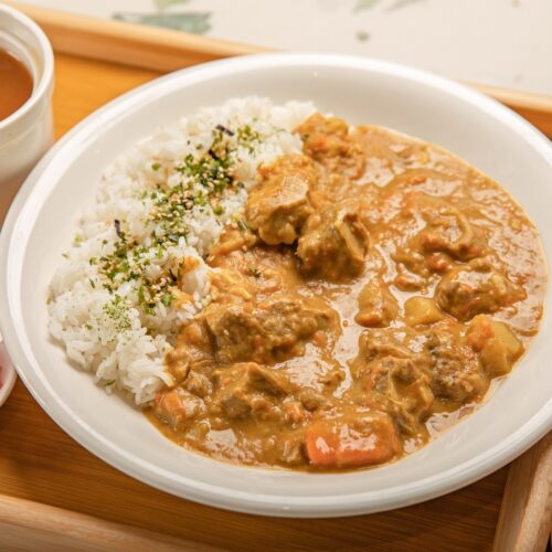 A savory Japanese curry with rice, served with soup and pickles on a wooden tray.