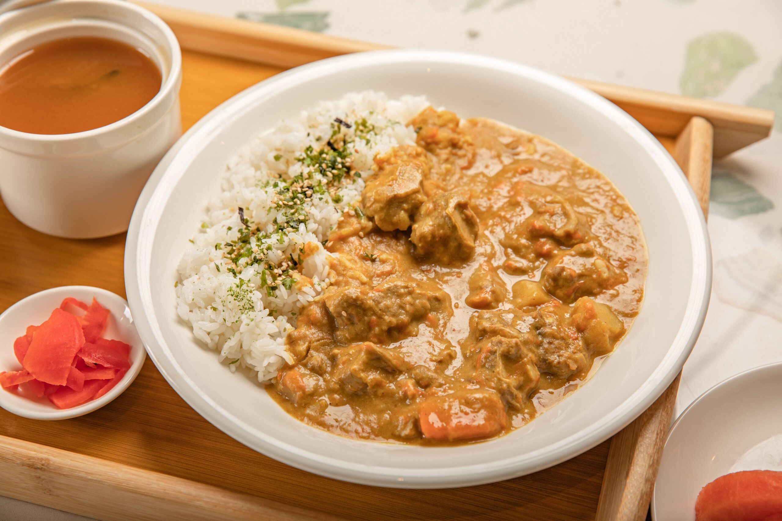 A savory Japanese curry with rice, served with soup and pickles on a wooden tray.