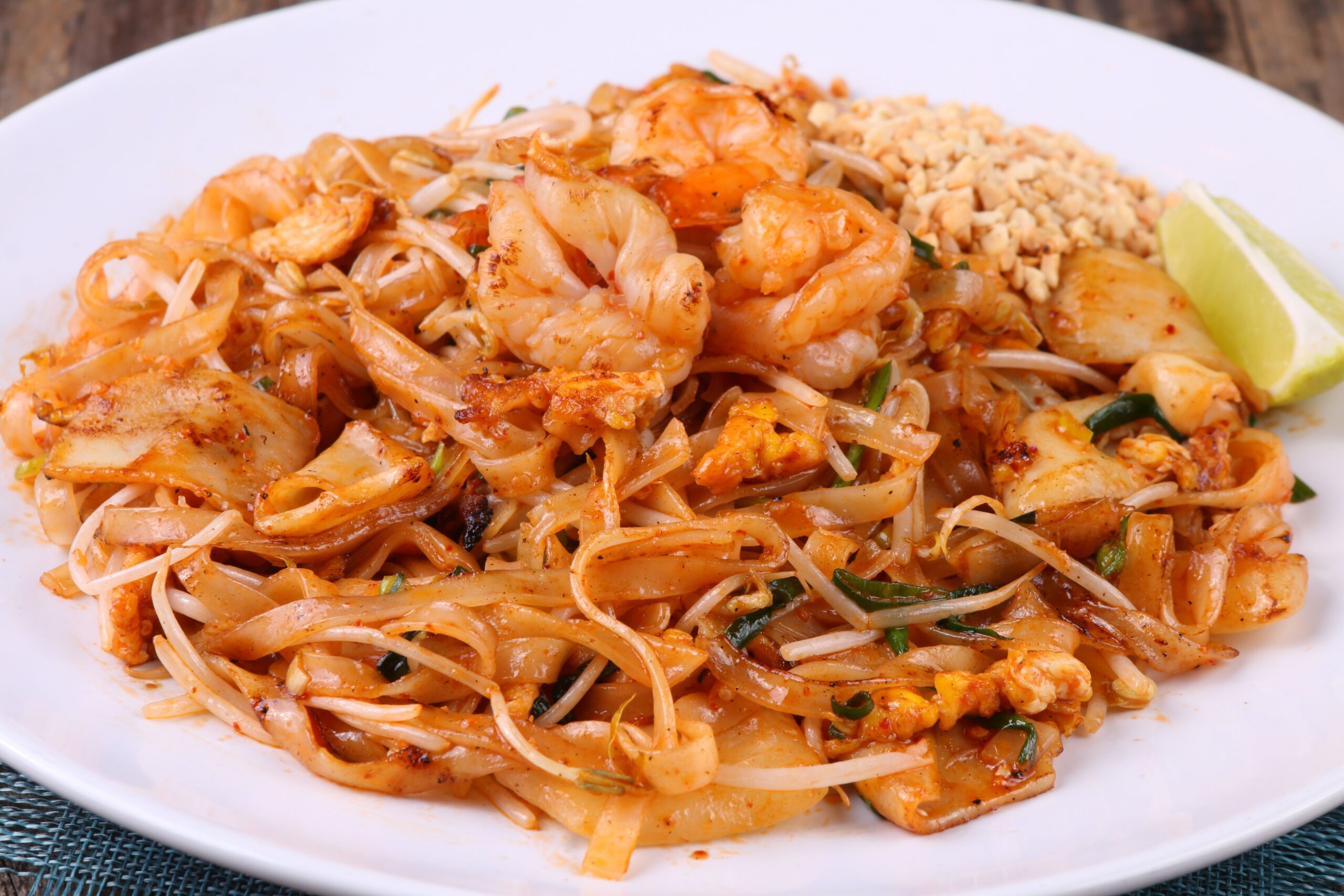 Close-up of shrimp pad thai with lime and peanuts on a white plate, perfect for food lovers.