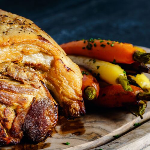 Delicious roast pork served with colorful carrots on a wooden board.